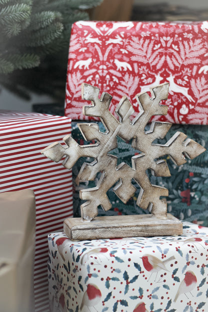 white washed mango wood snowflake on top of christmas presents in nostalgic style wrapping paper