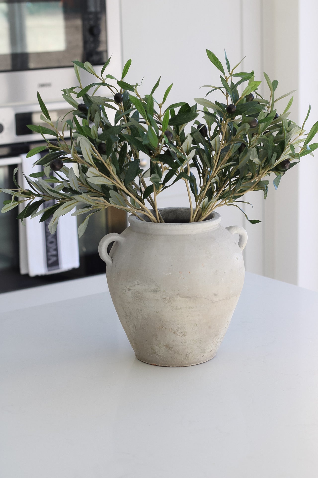 Tall grey olive pot with little handles, pot is filled with faux olive stems