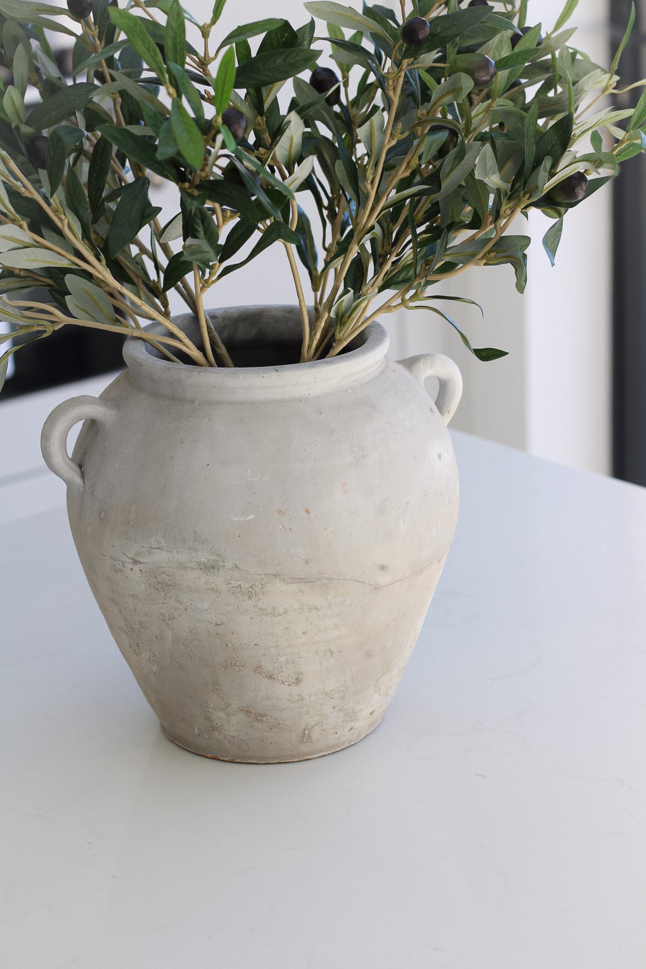 Tall grey olive pot with little handles, pot is filled with faux olive stems