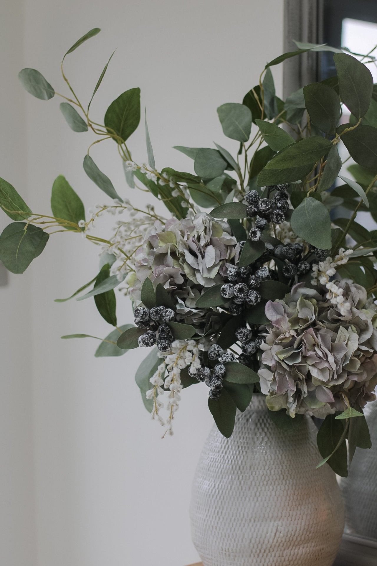 up close of faux pale lavender hydrangea and white willow flower arrangement. Pair with beautiful grey ceramic vase to display your faux flowers. A lovely addition to your christmas decor.