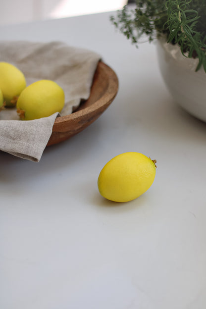 Decorative Faux Lemon on white worktop with wooden bowl in background