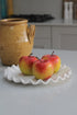 Faux Fuji Apple styled on white ceramic ruffled plate on kitchen worktop