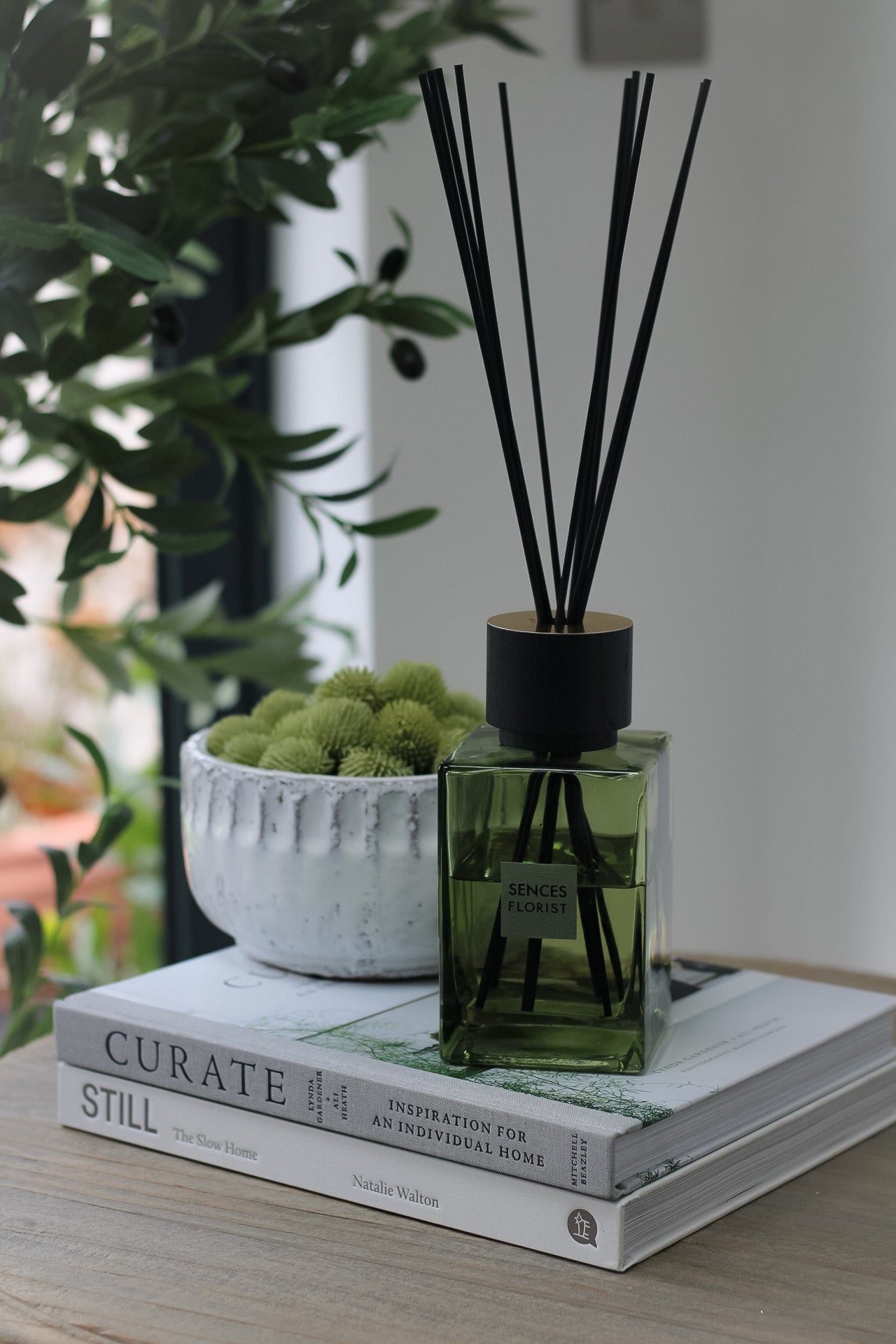 luxury reed diffuser styled on coffee table books with rustic bowl filled with faux textured balls