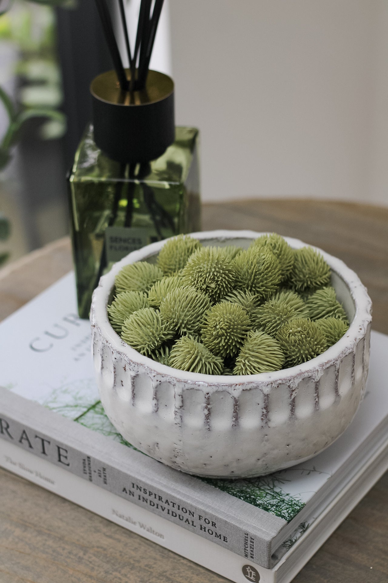 organic textured Green Echinops Balls styled in cream ceramic bowl on small side table with luxury reed diffuser